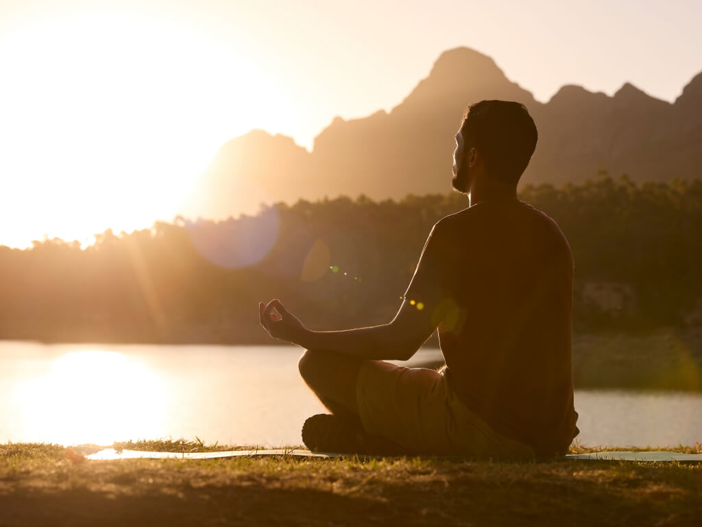 Man meditating near a lake with sunrise