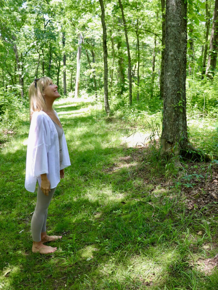 Regan standing in woods looking up at trees