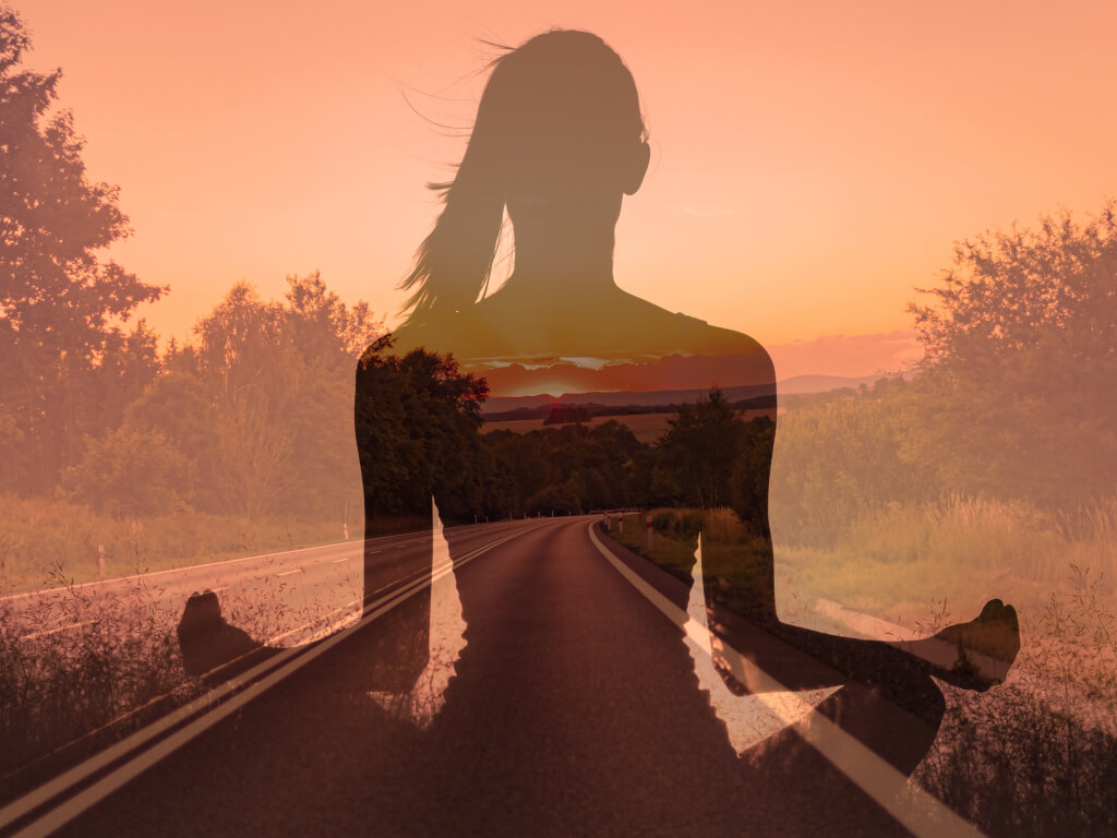 Silhouette of woman meditating superimposed on image of road leading to sunrise